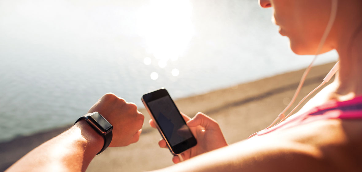 Woman beside the water, looking at her watch and holding a music player