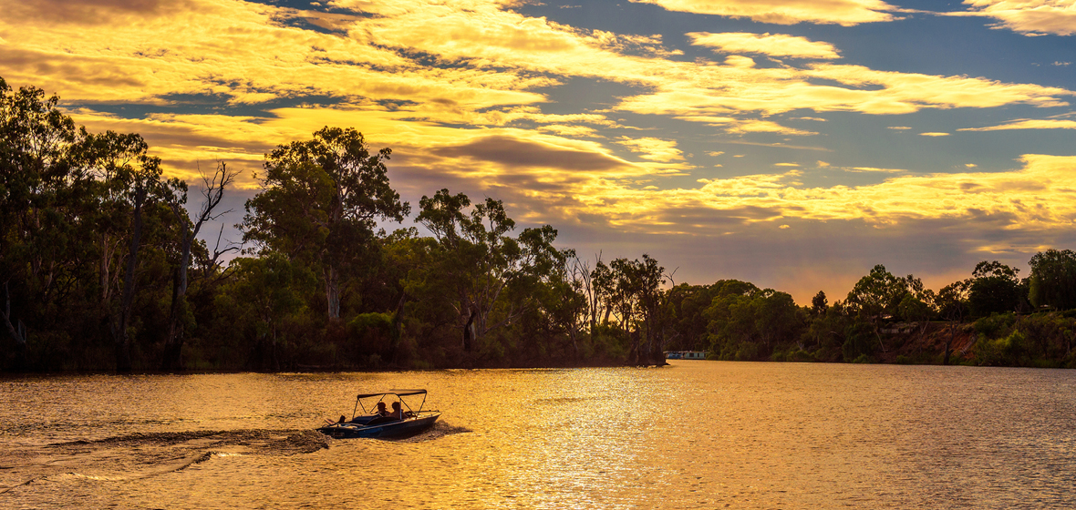 Bush surrounding a lake at sunset. A small boat sails across the lake.