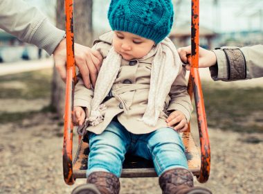 Child on a swing being pushed by two adults