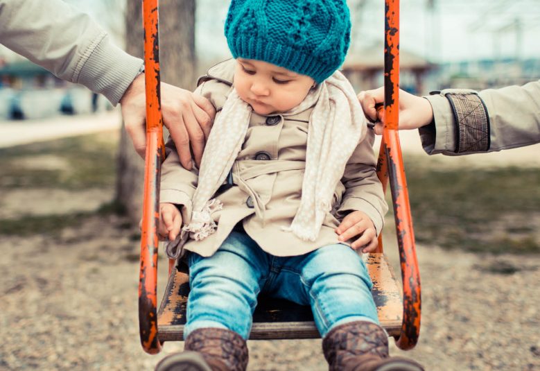 Child on a swing being pushed by two adults