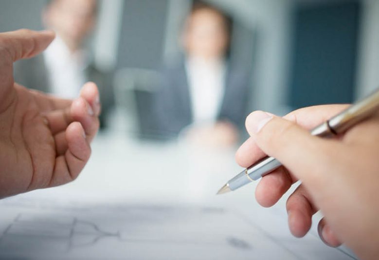 A person writes on a document while attending a meeting