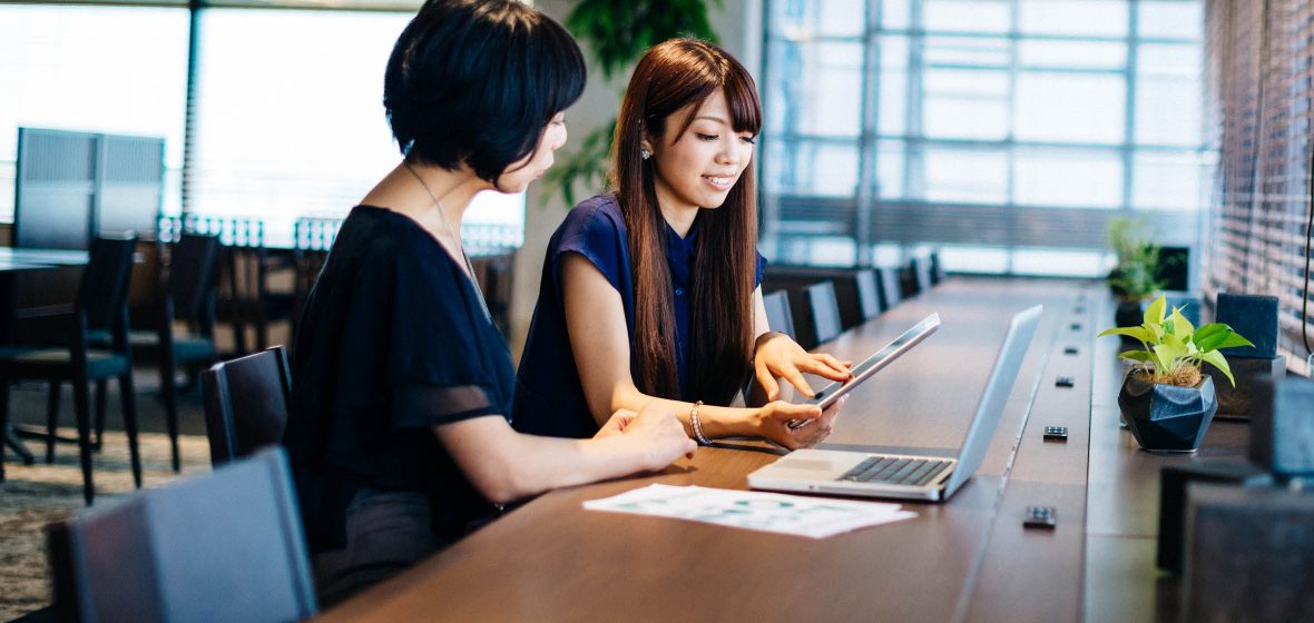 Two women with a laptop and a tablet sitting at a desk