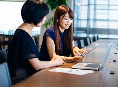 Two women with a laptop and a tablet sitting at a desk