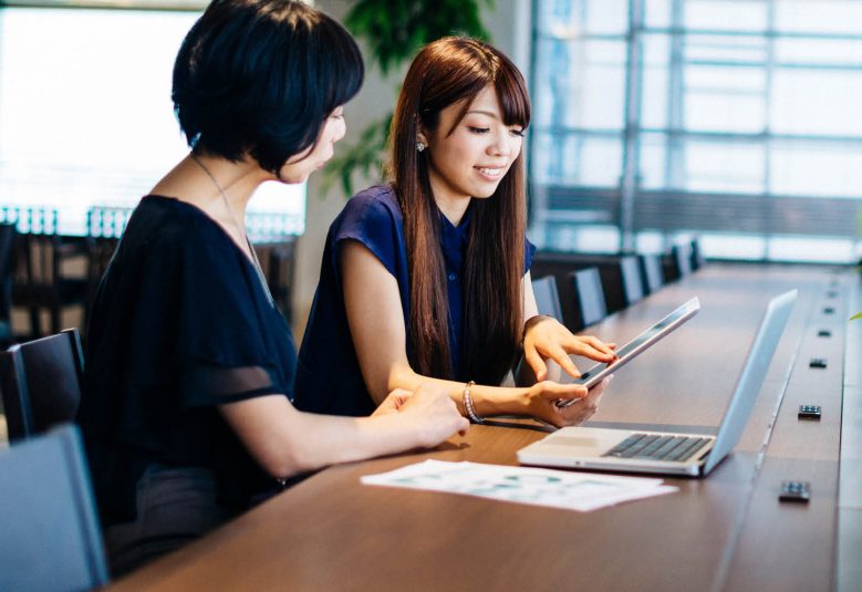 Two women with a laptop and a tablet sitting at a desk