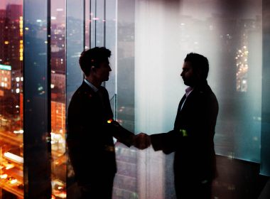 Two men shake hands in a darkened office