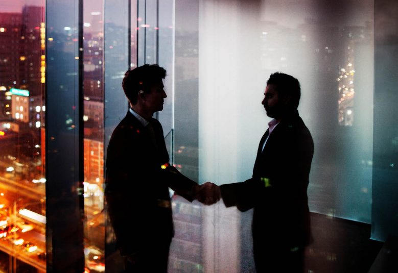 Two men shake hands in a darkened office