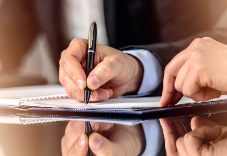 Man signs a document, witness by a second man