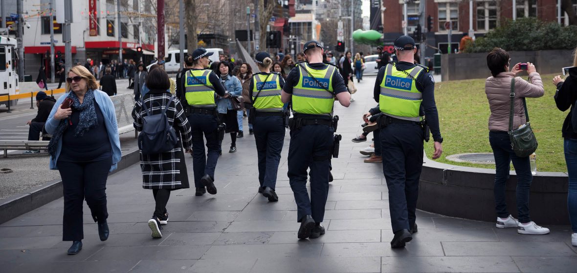 Four police walking down a street among pedestrians