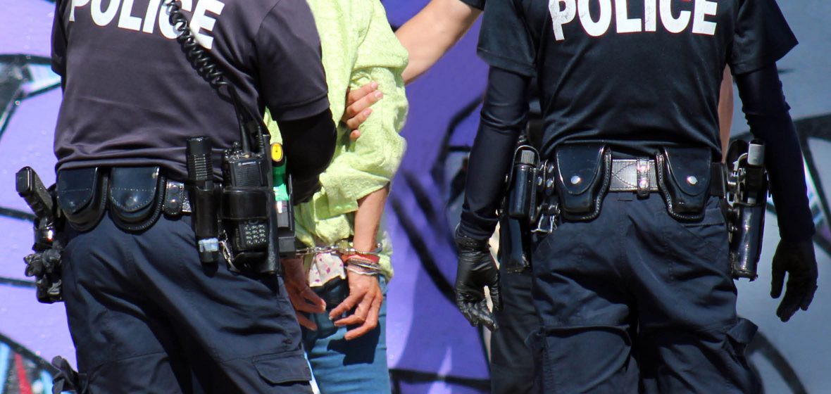 three police officers escorting a handcuffed male