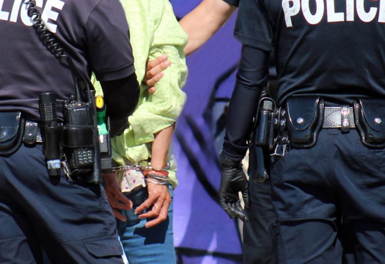 three police officers escorting a handcuffed male