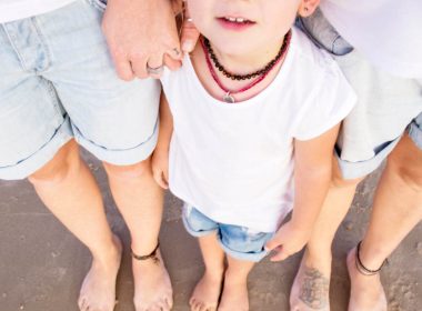 Two adults stand with a child on a beach.