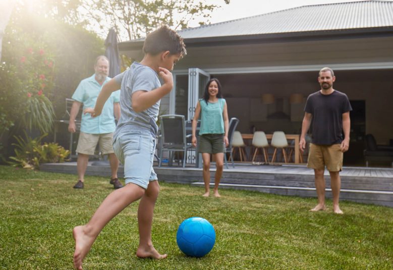 Child playing soccer with family in backyard of house