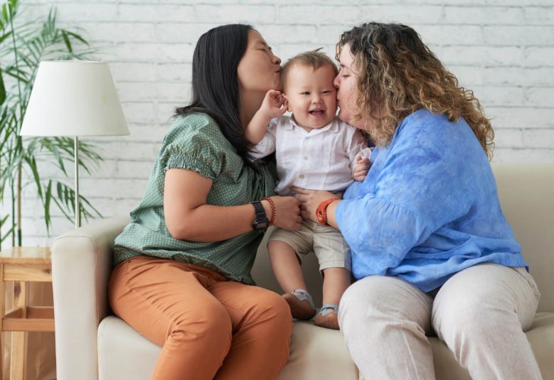 Two women sitting on the couch holding a child