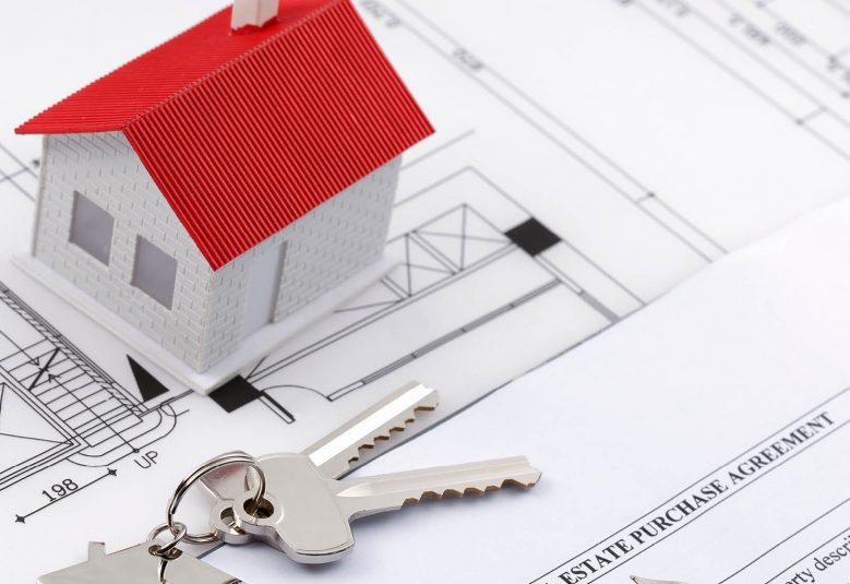 Scale model of house sits on housing plans next to a set of keys