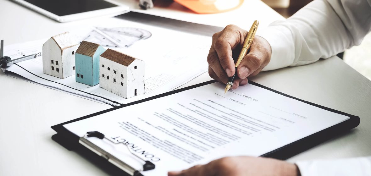 Man signs a contract on a desk, next to scale models of houses