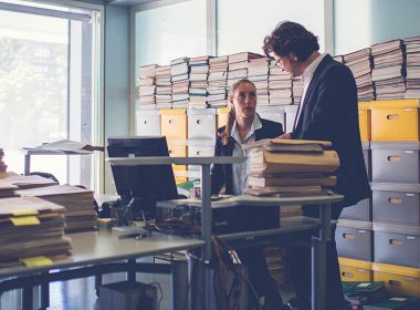 Man and woman in an office surrounded by boxes of files