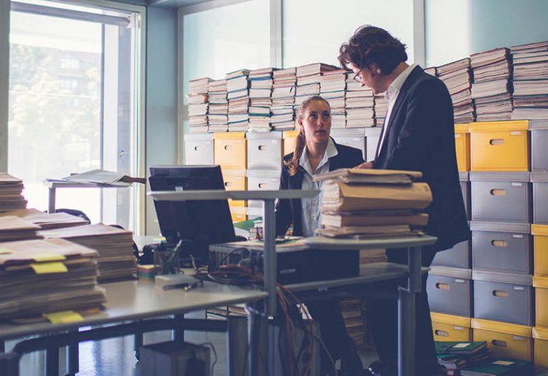 Man and woman in an office surrounded by boxes of files