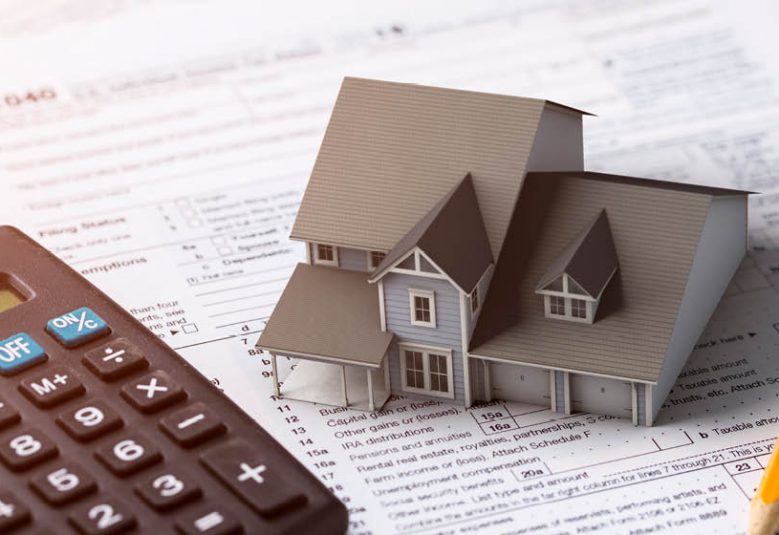 Model of a house on a desk with a calculator, pencil and financial paperwork