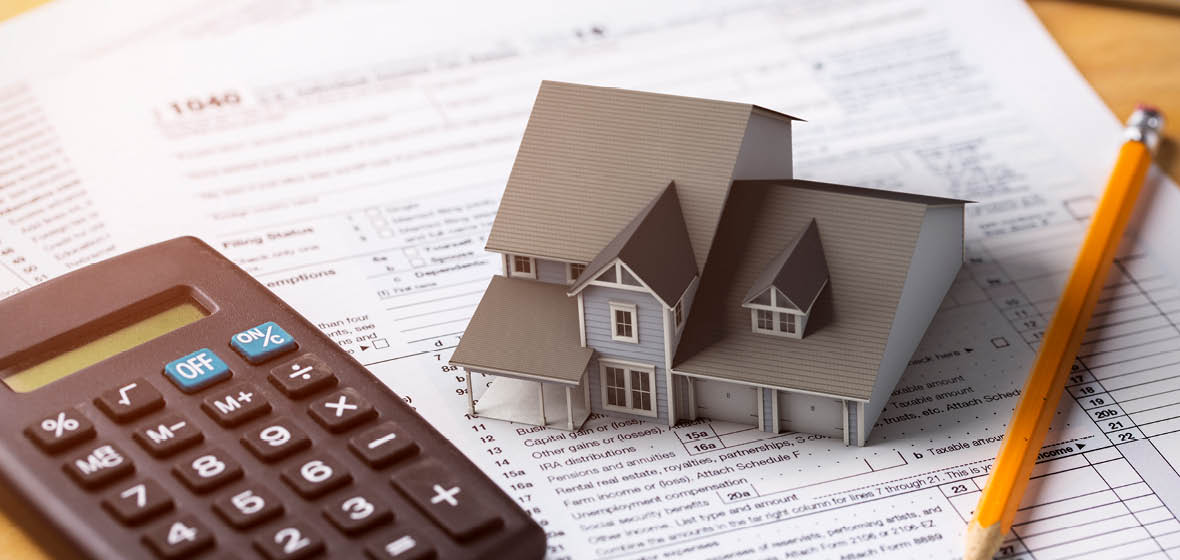 Model of a house on a desk with a calculator, pencil and financial paperwork