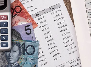 Calculator, Australian bank notes and a bank statement on a desk, next to a laptop