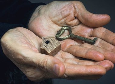 Older person's hands holding a key and a small wooden house