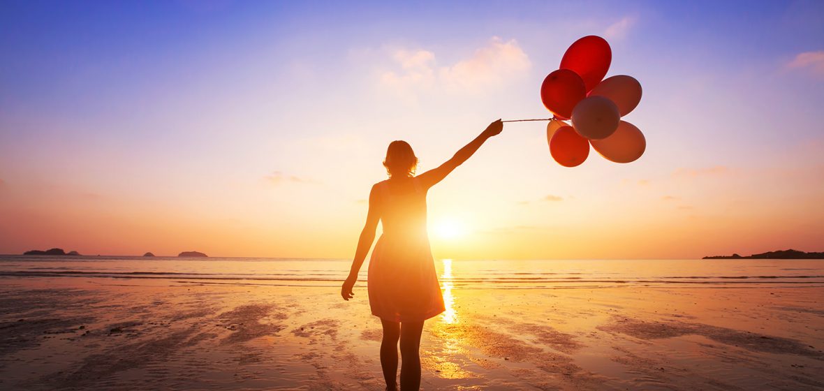 happy girl with multicolored balloons enjoying summer beach at sunset
