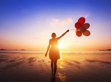 happy girl with multicolored balloons enjoying summer beach at sunset