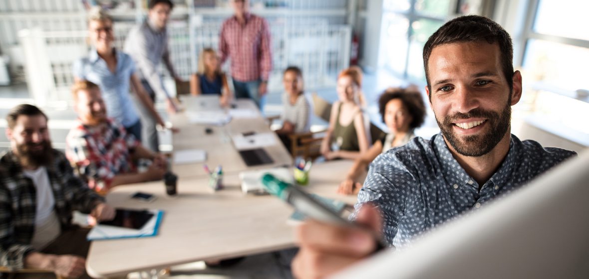 Happy businessman writing a business plan on whiteboard to his team on a meeting in board room