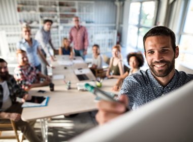 Happy businessman writing a business plan on whiteboard to his team on a meeting in board room