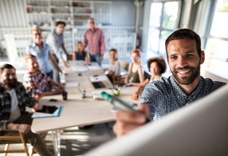 Happy businessman writing a business plan on whiteboard to his team on a meeting in board room