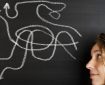 Woman's face next to a blackboard with several chalk arrows on it, pointing in different directions