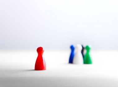 Board game pawns on wooden table. One pawn is positioned away from the others.