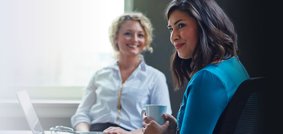 two women seated at a desk talking over coffee