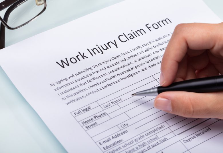 Close-up Of A Woman's Hand Filling Work Injury Claim Form