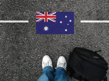 a man with a shoes and backpack is standing on asphalt next to flag of Australia and border