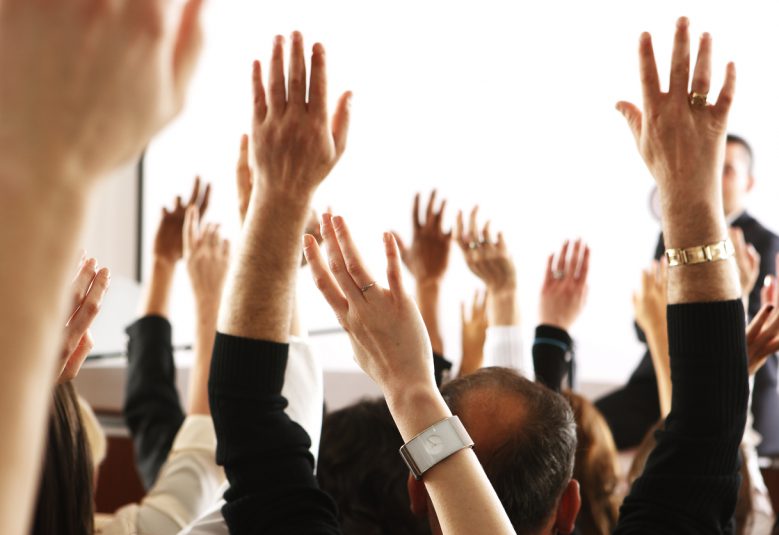 Big audience of people raising their hands to vote in favor of a topic.