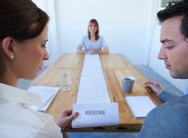 Two employers review a very long resume in front of a smiling candidate