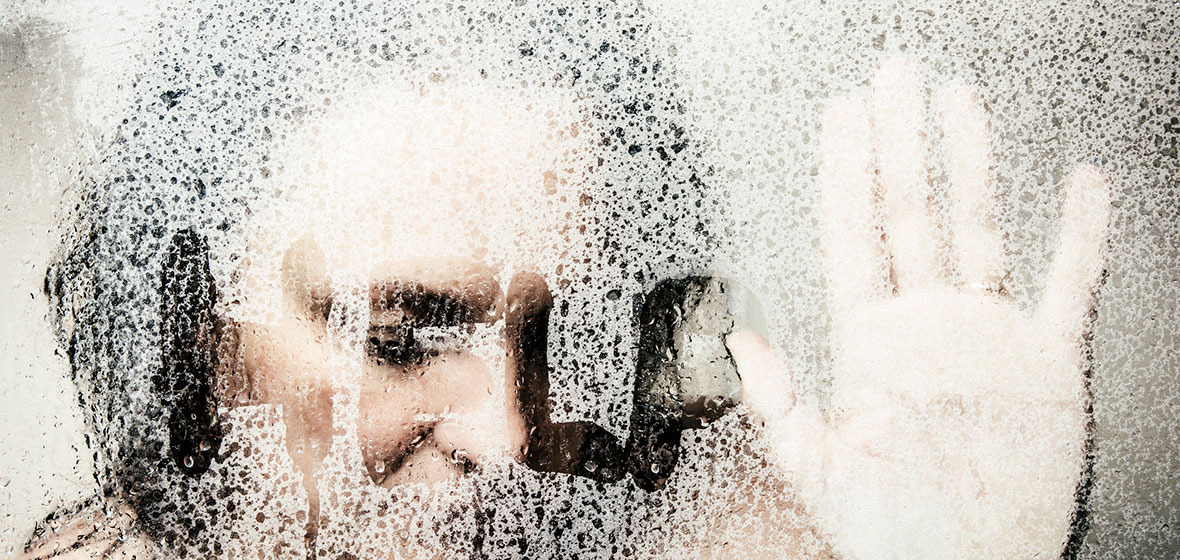 Woman with hand on glass, next to where she has written the word 'Help"