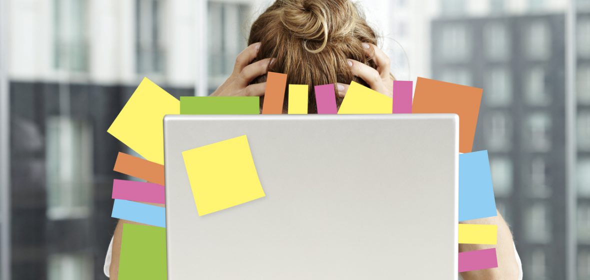 Exhausted businesswoman sits in front of a laptop covered in post-it notes