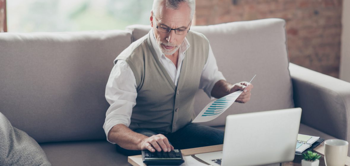 Man sitting on a couch, using a laptop and calculator