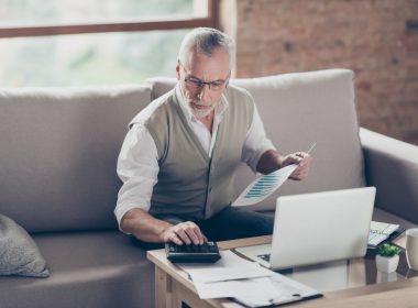 Man sitting on a couch, using a laptop and calculator