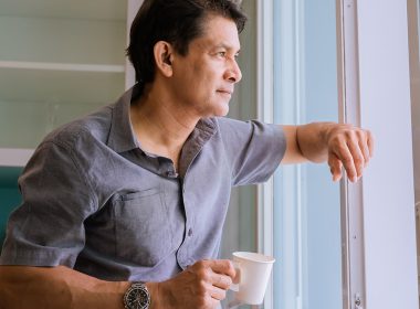 Middle-aged Asian man looking through a window, sipping coffee