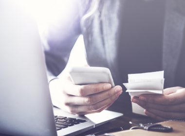 Person reviewing receipts at a desk with a laptop and mobile phone