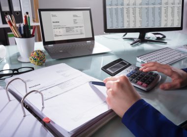 Person using a calculator reads an invoice at a desk