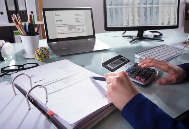 Person using a calculator reads an invoice at a desk