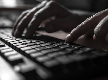 Fingers typing on a keyboard in a dark room