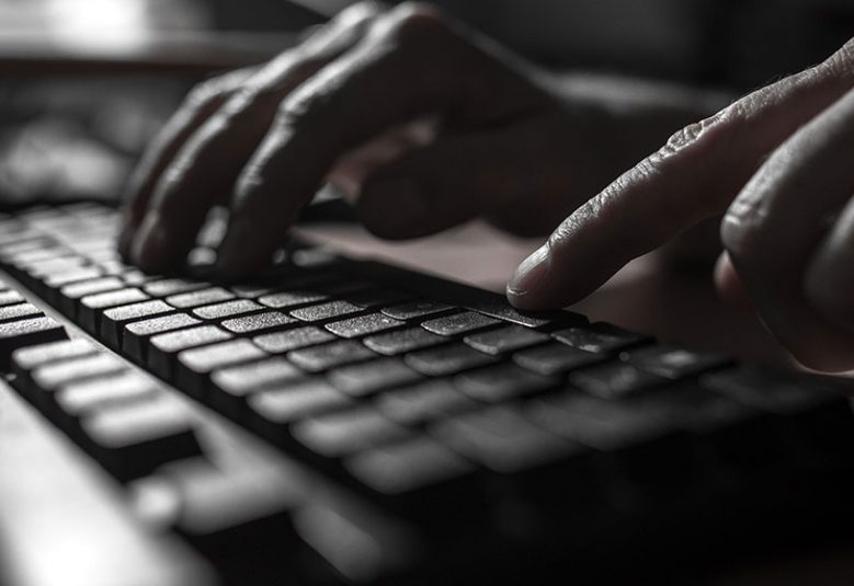 Fingers typing on a keyboard in a dark room