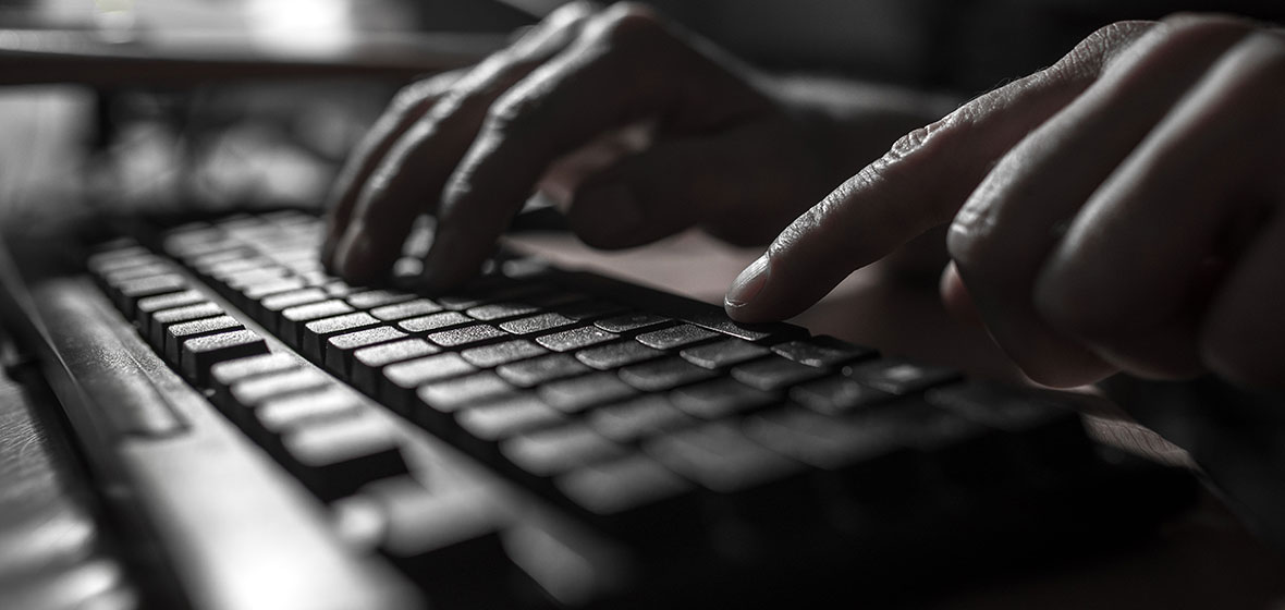 Fingers typing on a keyboard in a dark room