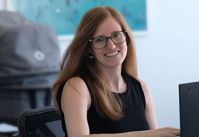 photo of lawyer Rafaella at her desk with baby pram in the background to show she is on parental leave