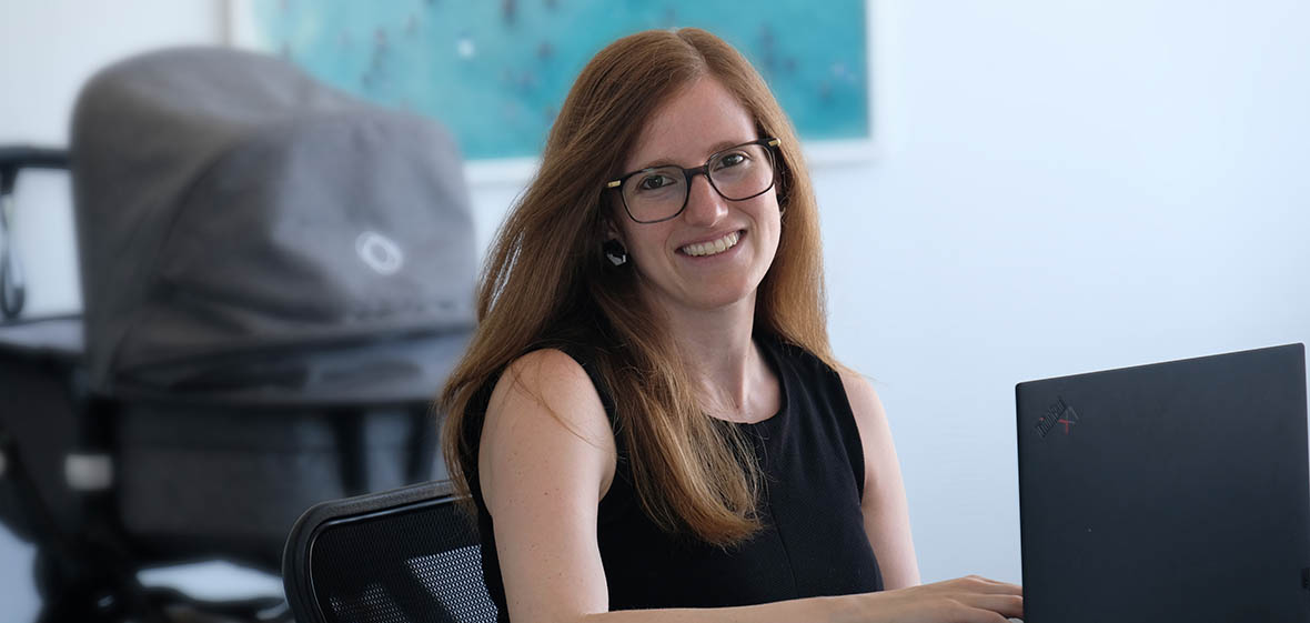 photo of lawyer Rafaella at her desk with baby pram in the background to show she is on parental leave